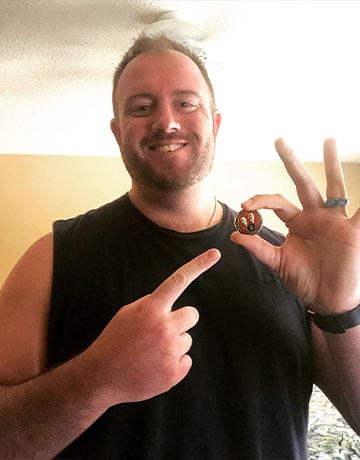 sober living outcomes | happy smiling sober living resident holding his two year sober anniversary celebration coin