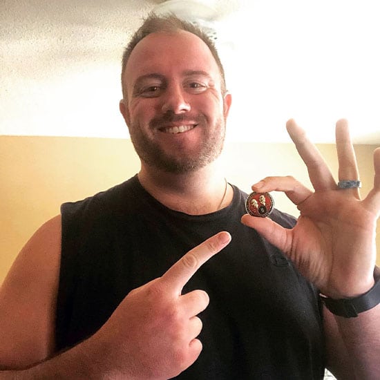 sober living outcomes | happy smiling sober living resident holding his two year sober anniversary celebration coin mobile