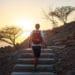 Image of a young man hiking up steps on a mountain trail with the sunsetting in front of him, beautiful scenery representing the journey on men in sobriety and the 12-step recovery program.